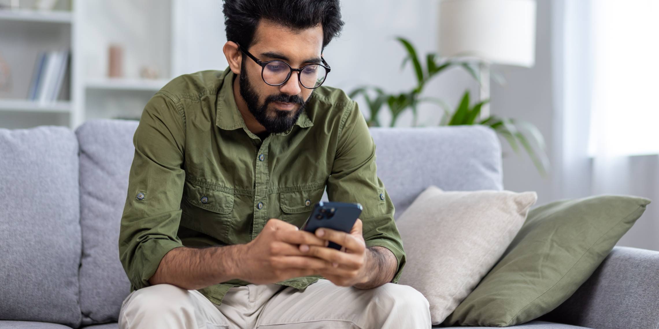 man with glasses looking at mobile phone while sitting on a sofa